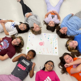 Girls on the Run in a circle on the ground with a poster made during practice